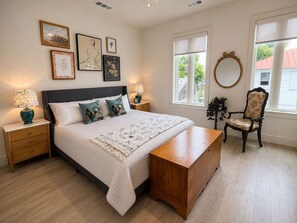 Ein Schlafzimmer mit Bett, Nachttischen, einem Sessel, einem Spiegel und Bildern an der Wand.