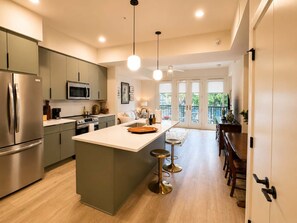 A modern kitchen with a central island, stainless steel appliances, and a dining area with bar stools. - The Jardin Briar Suite | Near Downtown (Savannah)