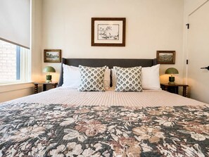 A hotel room with a large bed, two nightstands, a window, and a framed picture on the wall. - The Jardin Briar Suite | Near Downtown (Savannah)