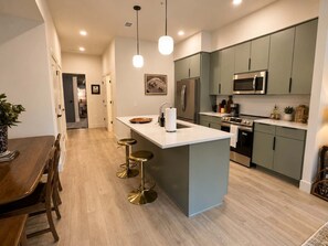 A modern kitchen with a central island, stainless steel appliances, and a dining area with wooden furniture. - The Jardin Briar Suite | Near Downtown (Savannah)