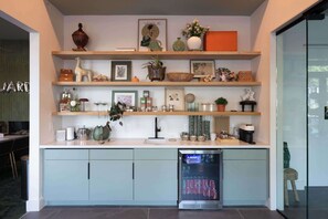 Eine Küche mit Kühlschrank, Regalen mit diversen Gegenständen und einem Essbereich im Hintergrund.