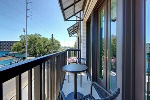 Een balkon met een tafel en stoelen, met uitzicht op een straat met gebouwen en bomen.