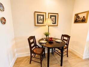 A dining area with a round table, two chairs, a lamp, and framed artwork on the wall. - The Jardin Elm Suite | Near Downtown (Savannah)