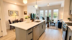 Eine moderne Küche mit Kochinsel, ein Essbereich mit Tisch und Stühlen sowie ein Wohnbereich mit Sofa und Couchtisch.