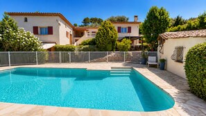 Ein Swimmingpool mit Fliesen umrandet, umzäunt und neben Gebäuden mit roten Fensterläden gelegen.