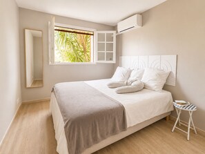 Ein Schlafzimmer mit Bett, einem Fenster mit Blick auf Grünflächen, einem Nachttisch und einer Klimaanlage.