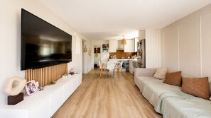 Ein modernes Wohnzimmer mit Flachbildfernseher, einer Couch und einem Essbereich mit Tisch und Stühlen.