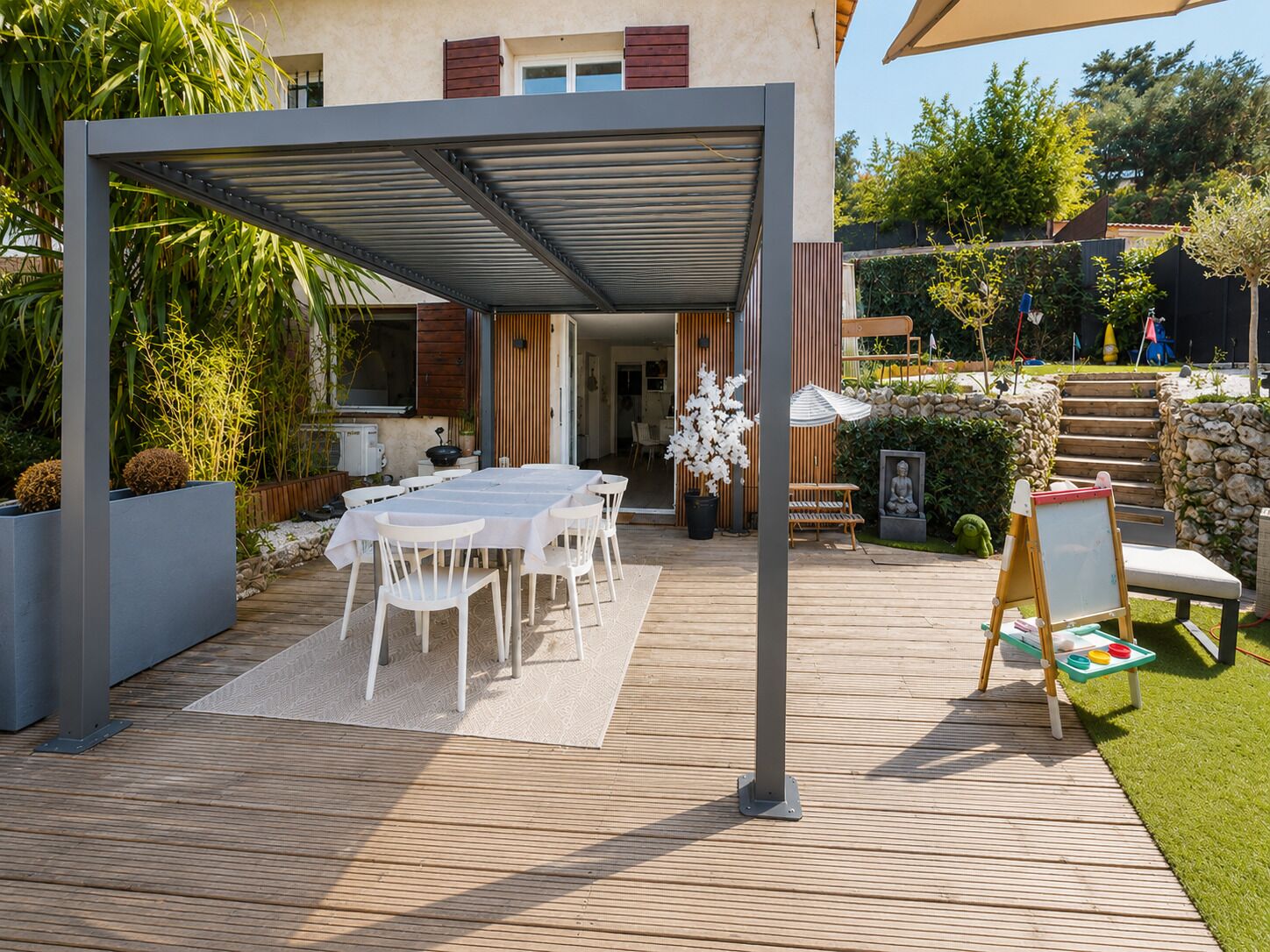 Une terrasse extérieure dotée d’un espace repas couvert, d’une terrasse en bois et d’un mur en pierre.