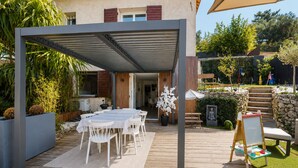 En udendørs terrasse med et overdækket spiseområde, en træterrasse og en stenvæg.
