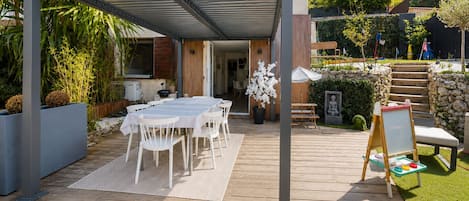 Une terrasse extérieure dotée d’un espace repas couvert, d’une terrasse en bois et d’un mur en pierre.