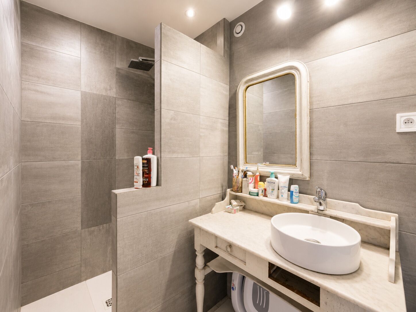A modern bathroom with a large mirror, a round sink, and a shower area.