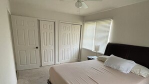 Quarto com cama, ventilador de teto e janela com persianas.