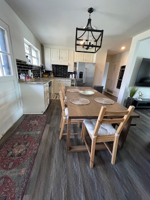 A modern kitchen with white cabinets, a stainless steel refrigerator, and a dining area with a wooden table and chairs. - Charming 3-bedroom house (Euless)