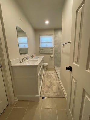 A narrow bathroom with a double sink vanity, a toilet, and a shower area. - Charming 3-bedroom house (Euless)