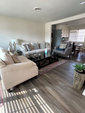 A living room with a sofa, coffee table, and a dining area with a table and chairs. - Charming 3-bedroom house (Euless)
