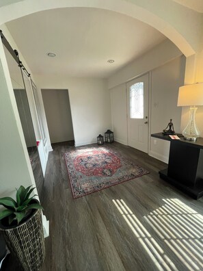 A hallway with a patterned rug, a door with a window, a lamp, and a small statue on a table. - Charming 3-bedroom house (Euless)