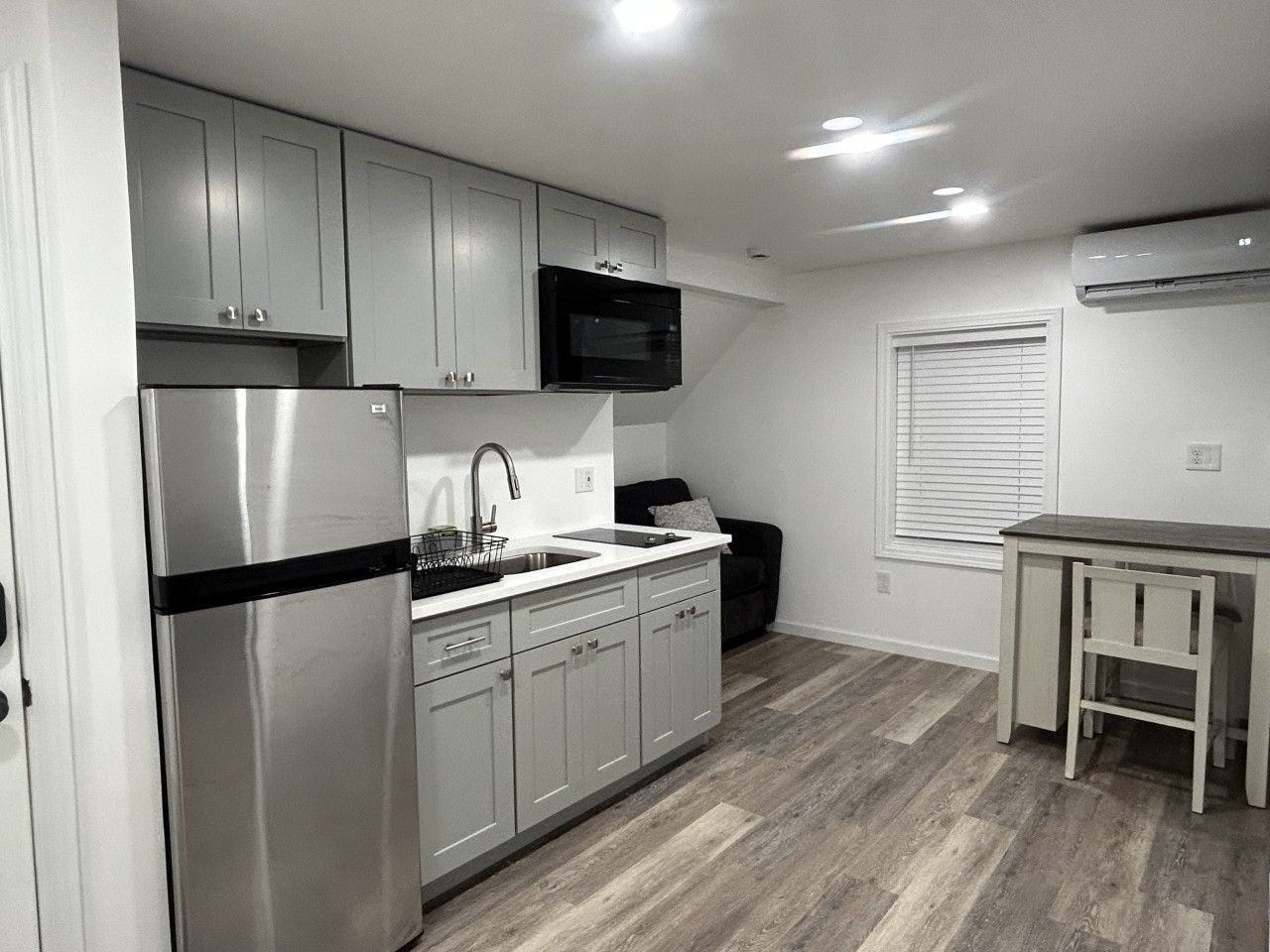 A modern kitchen with stainless steel appliances, white cabinetry, and a wooden floor.