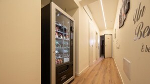 Een gang met een automaat vol verschillende producten, een deur aan het einde en een muur met een gedeeltelijke tekst.
