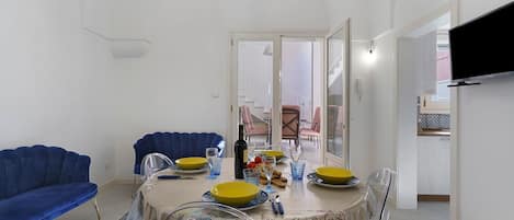 A dining area with a table set for four, a blue sofa, and a television mounted on the wall.