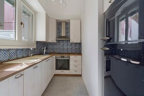 Una cocina compacta con horno integrado, una ventana con detalles decorativos y un salpicadero de azulejos.