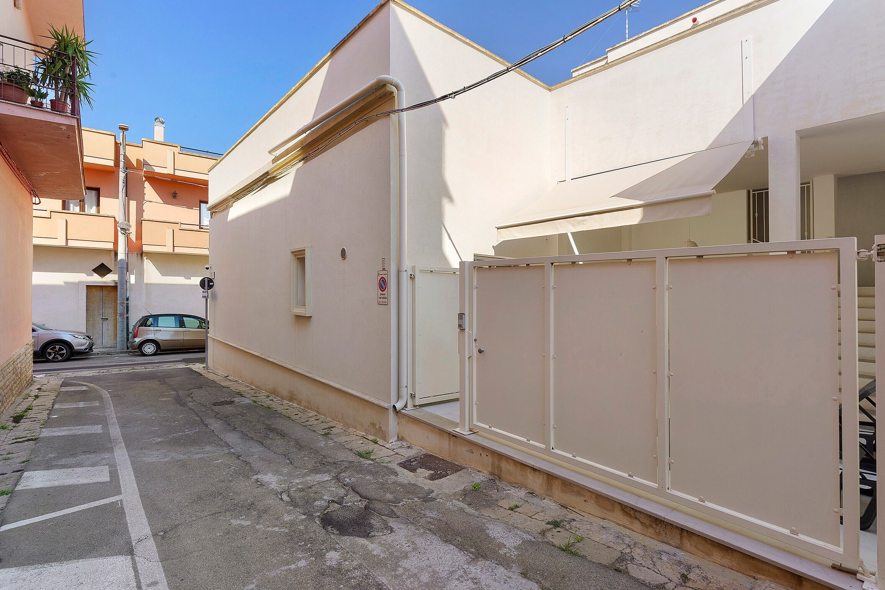 A narrow street with a parked car and a building with a gated entrance.