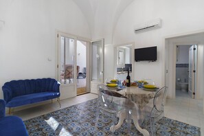 Una sala de estar moderna con un sofá azul, una mesa de comedor preparada para cuatro personas y un televisor montado en la pared.