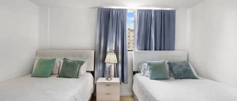 A twin room with two beds, a nightstand, a lamp, and a window with curtains.