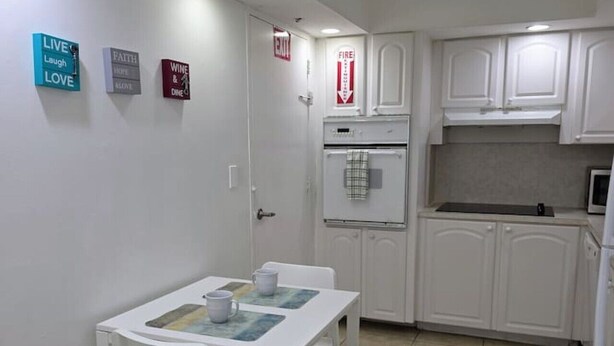 A compact kitchen with white cabinets, a built-in oven, and a small dining table with chairs. - Vive la experciencia frente al mar (Hollywood)