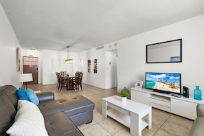 A modern living room with a sofa, a coffee table, a TV, and a dining area with chairs and a table. - Vive la experciencia frente al mar (Hollywood)