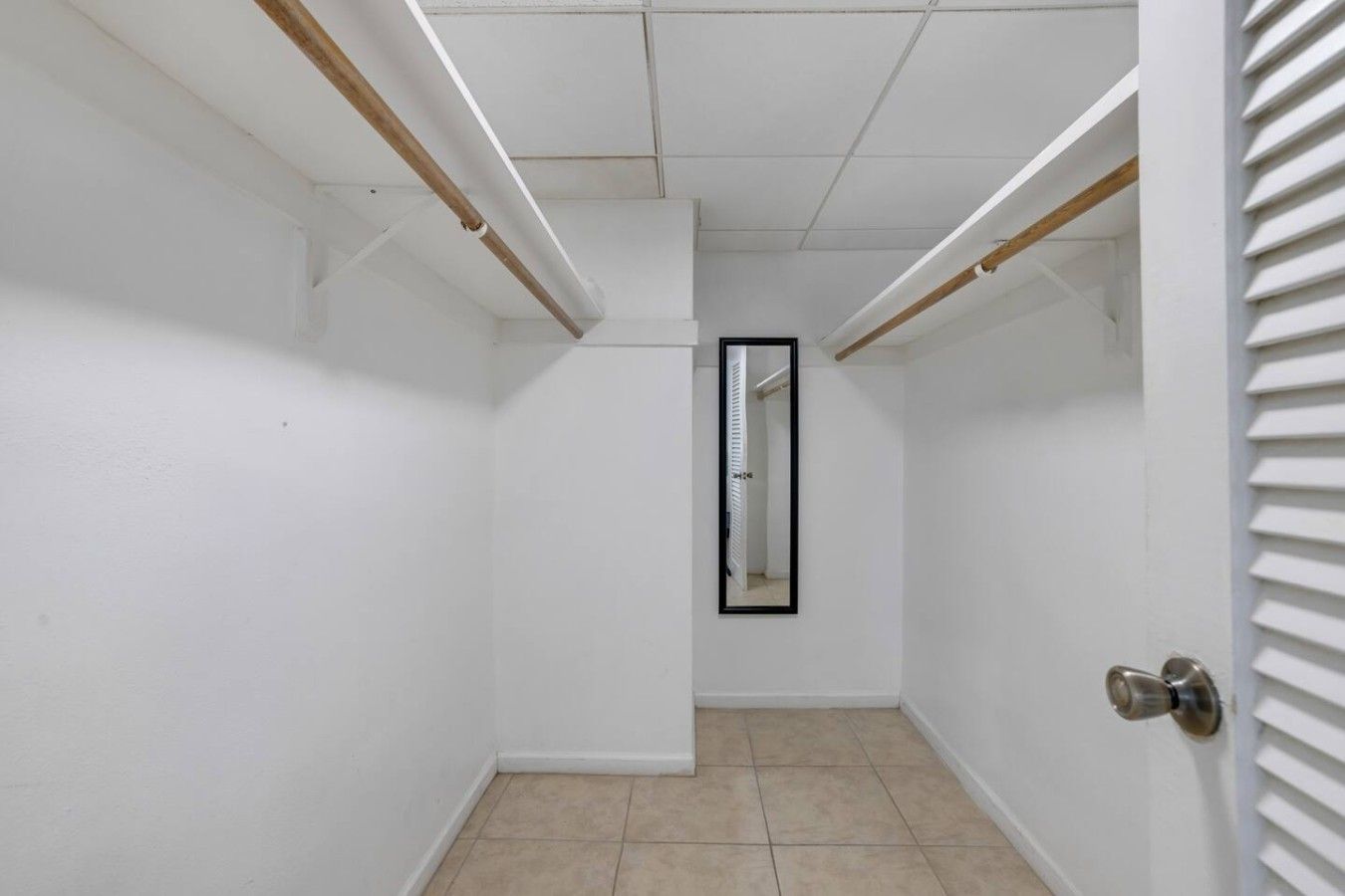 Un pasillo estrecho con paredes blancas, piso de baldosas y una puerta con manija de metal.