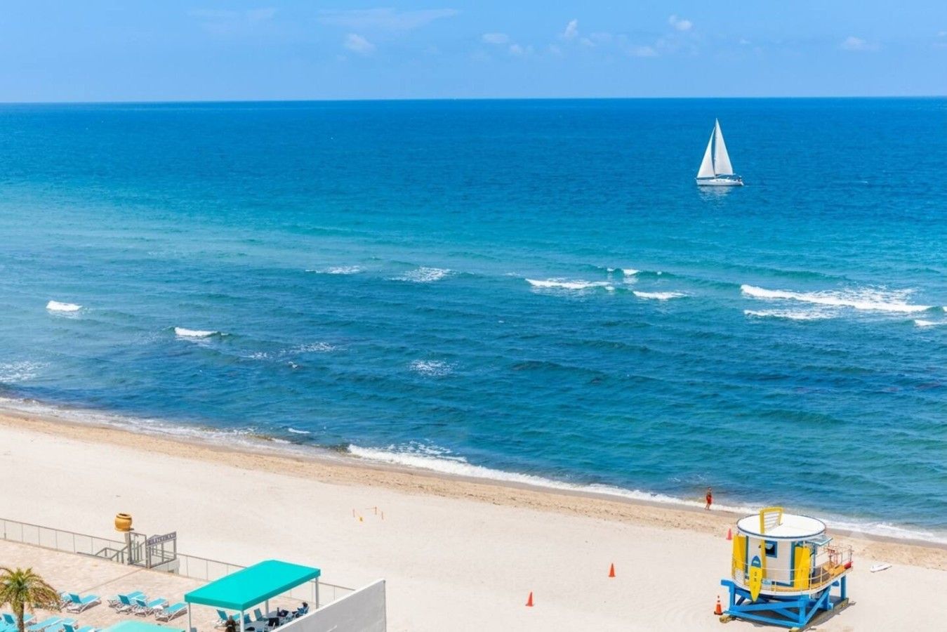 Una playa con una torre de salvavidas, un velero y un cielo azul despejado.