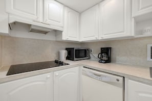 A kitchen with white cabinetry, a black induction cooktop, a microwave, a coffee maker, and a dishwasher. - Vive la experciencia frente al mar (Hollywood)