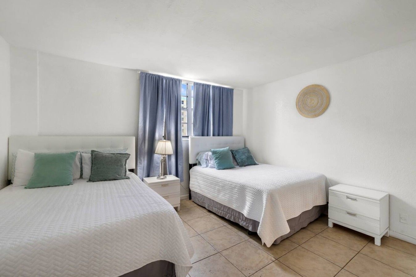 A bedroom with two beds, a nightstand with a lamp, and a wall-mounted decorative item.