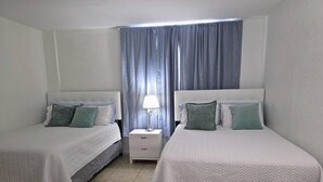 A hotel room with two beds, a nightstand, a lamp, and a window with curtains. - Vive la experciencia frente al mar (Hollywood)