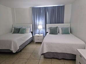 A hotel room with two beds, a nightstand, a lamp, and a window with curtains. - Vive la experciencia frente al mar (Hollywood)