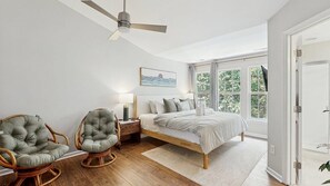 A bedroom with a bed, two chairs, a nightstand, a ceiling fan, and a window with a view of trees. - Rehoboth Crossing - 37063 Turnstone Cir (Rehoboth Beach)