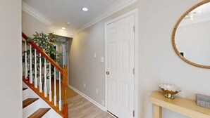 Un pasillo con una escalera de madera, puertas blancas y una consola con espejo.