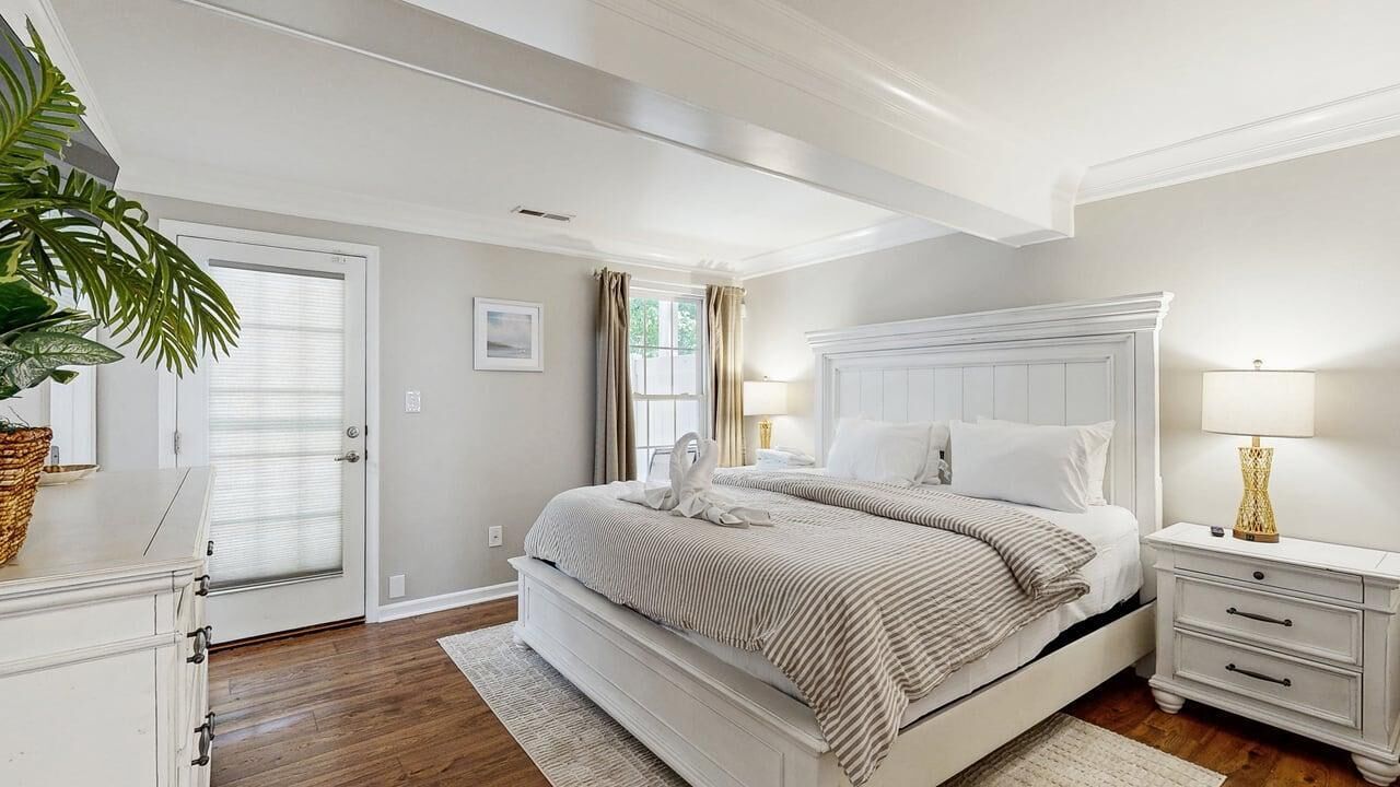 A bedroom with a large bed, bedside tables, a nightstand, a potted plant, and a window with curtains.