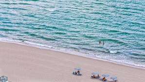 Una playa con gente en el agua y sillas de playa bajo sombrillas.
