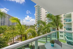 Ein Balkon mit Blick auf einen modernen Gebäudekomplex, Palmen und einen klaren Himmel.