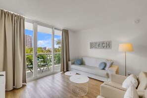 A modern living room with a sofa, two side tables, a lamp, and a balcony with a view of buildings and greenery. - Hollywood Escape |Piscina| Playa | Vistas | Balcón (Hollywood)