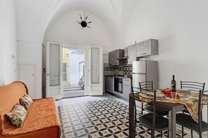 Un ambiente compatto con angolo cottura, zona pranzo con tovaglia fantasia e divano con cuscini decorati.