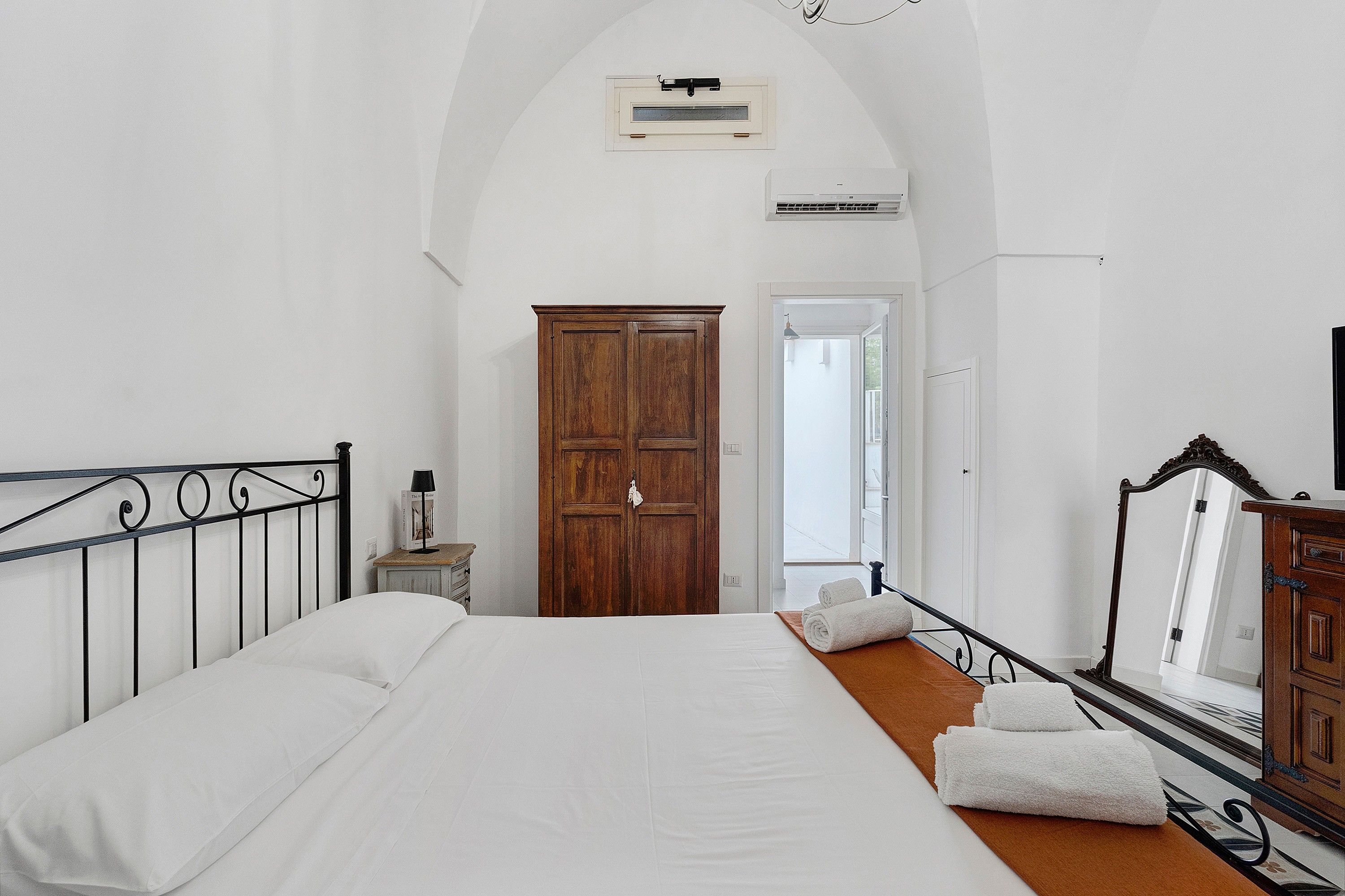 A bedroom with a large bed, a wooden wardrobe, and a door leading to a balcony.