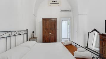Quarto com cama grande, guarda-roupa de madeira e porta para uma varanda.