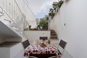 A narrow outdoor patio with a table set for two, a white railing, and a staircase leading to a balcony. - Dimora Collina 3 Apartment with Terrace, Wi-Fi, and Air Conditioning (Sannicola)