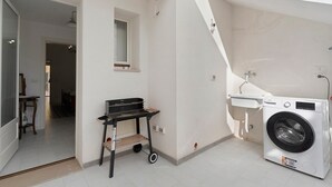 Een wasruimte met een wasmachine, een klein tafeltje en een bank.