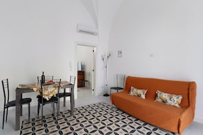 A dining area with a table set for four, a sofa, and a patterned floor. - Dimora Collina 3 Apartment with Terrace, Wi-Fi, and Air Conditioning (Sannicola)