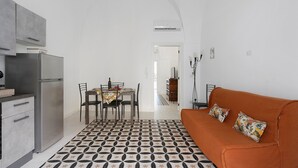 Een moderne keuken met een koelkast, eettafel en stoelen. De zithoek is voorzien van een bank met kussens.