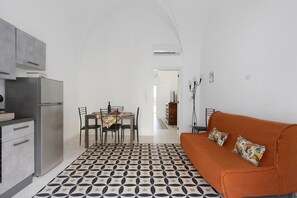Una cucina moderna con frigorifero, tavolo e sedie. Nell'area living, un divano con cuscini.