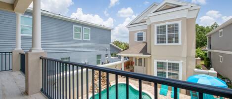 A residential property with a swimming pool, outdoor furniture, and a balcony with a railing.